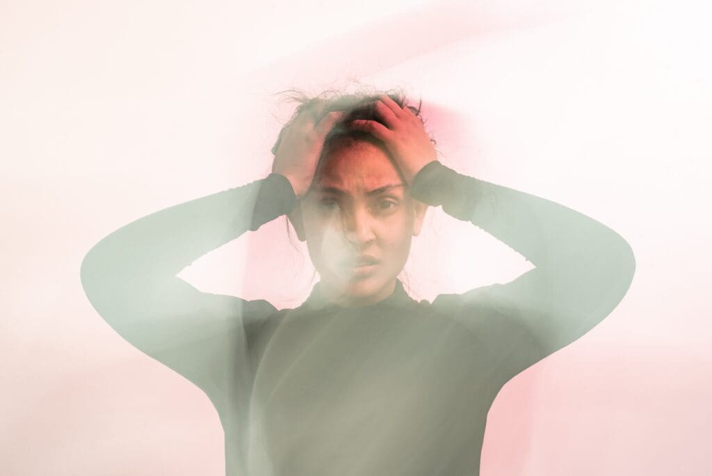 a woman in a black turtleneck sweater holds her hands to her head and looks confused