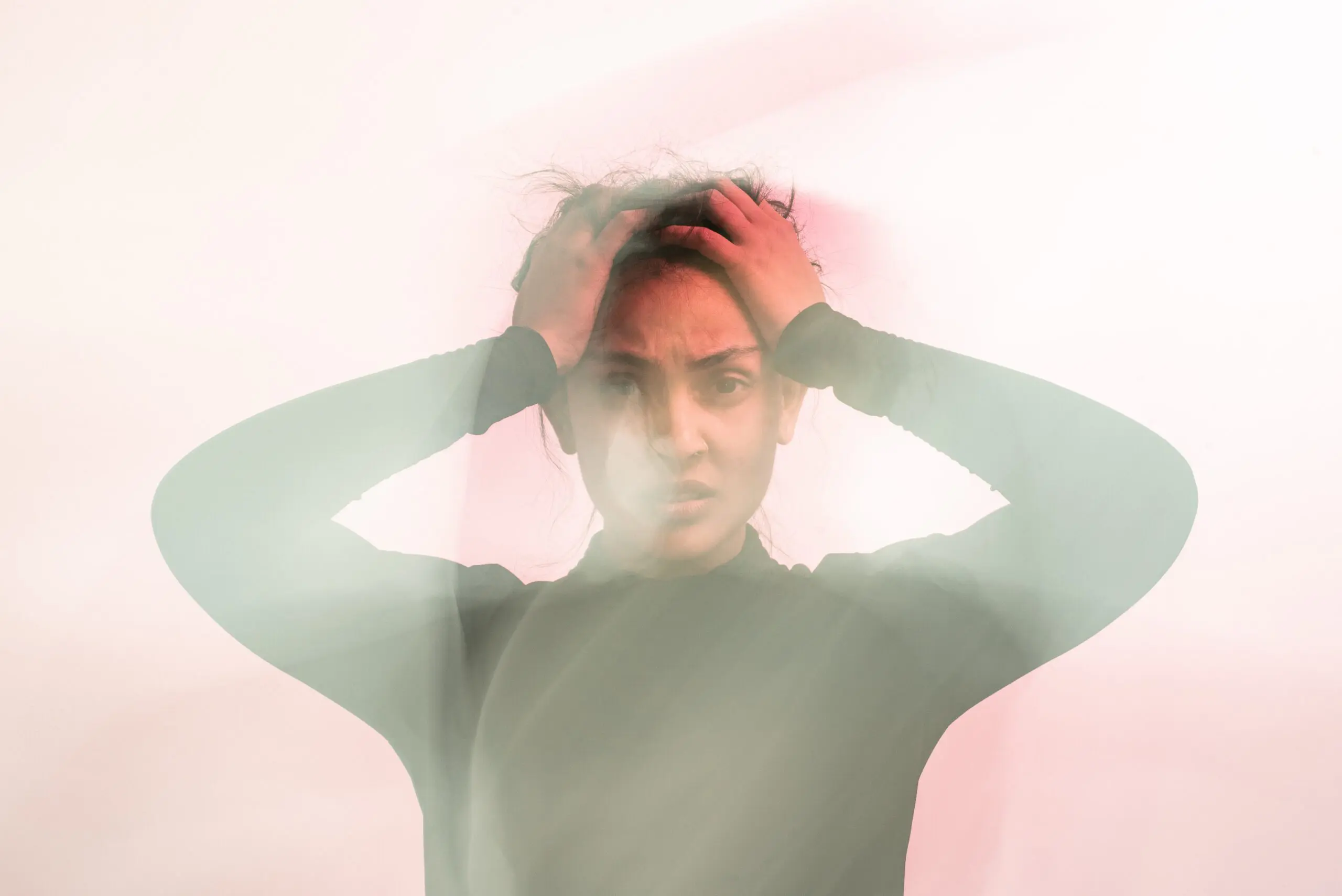 a woman in a black turtleneck sweater holds her hands to her head and looks confused