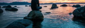 a person sits on a rock in a river at sunset and practices interoception and mindfulness