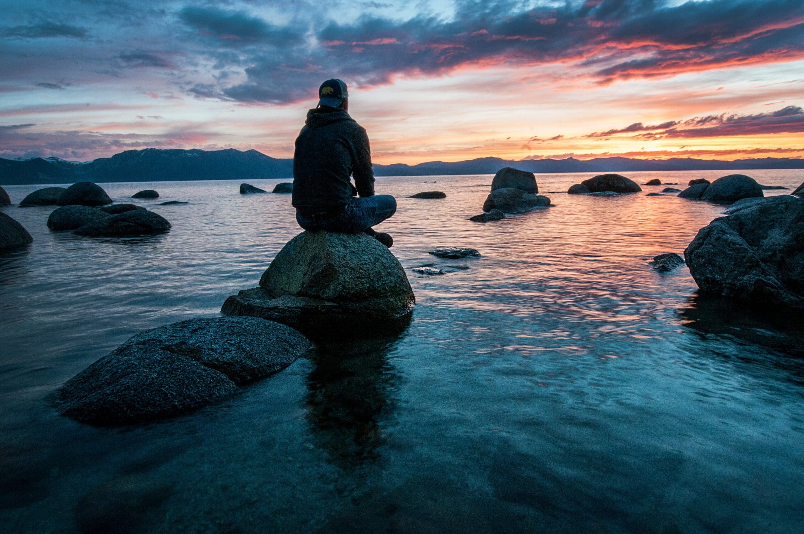 a person sits on a rock in a river at sunset and practices interoception and mindfulness