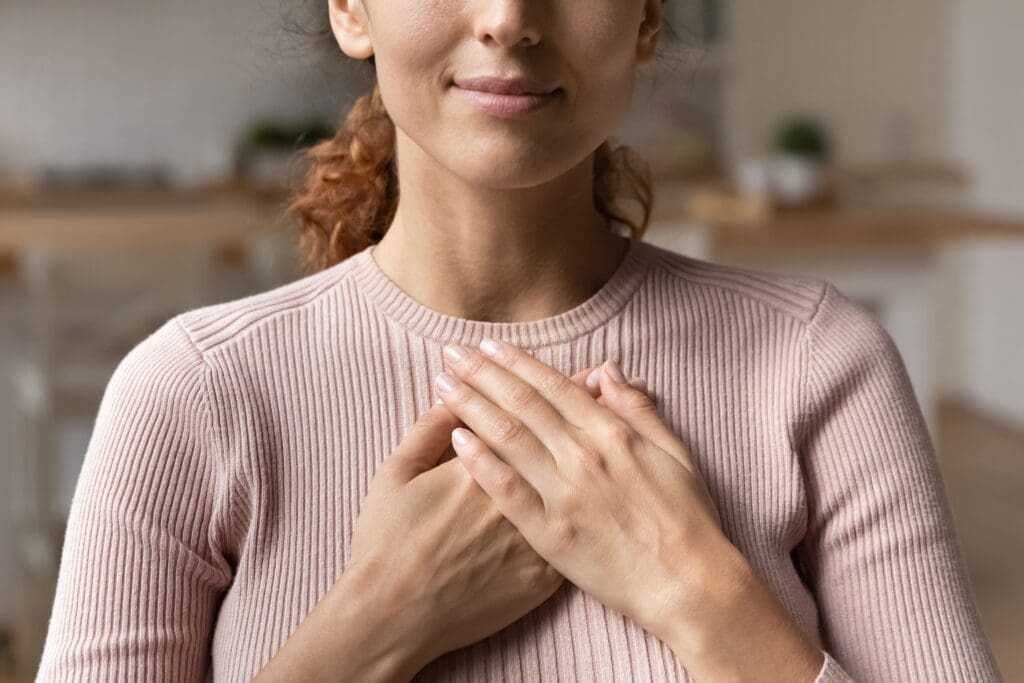 A close-up image of a woman holding her hands over her chest in a comfortable position