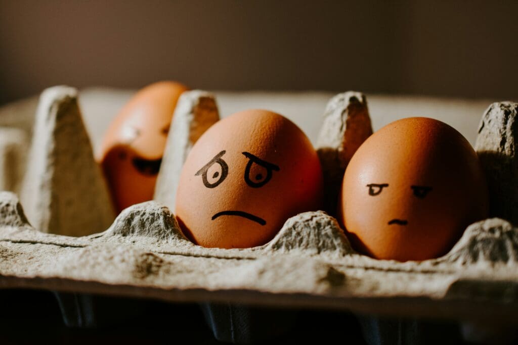 Eggs in a carton with worried faces drawn on them with marker