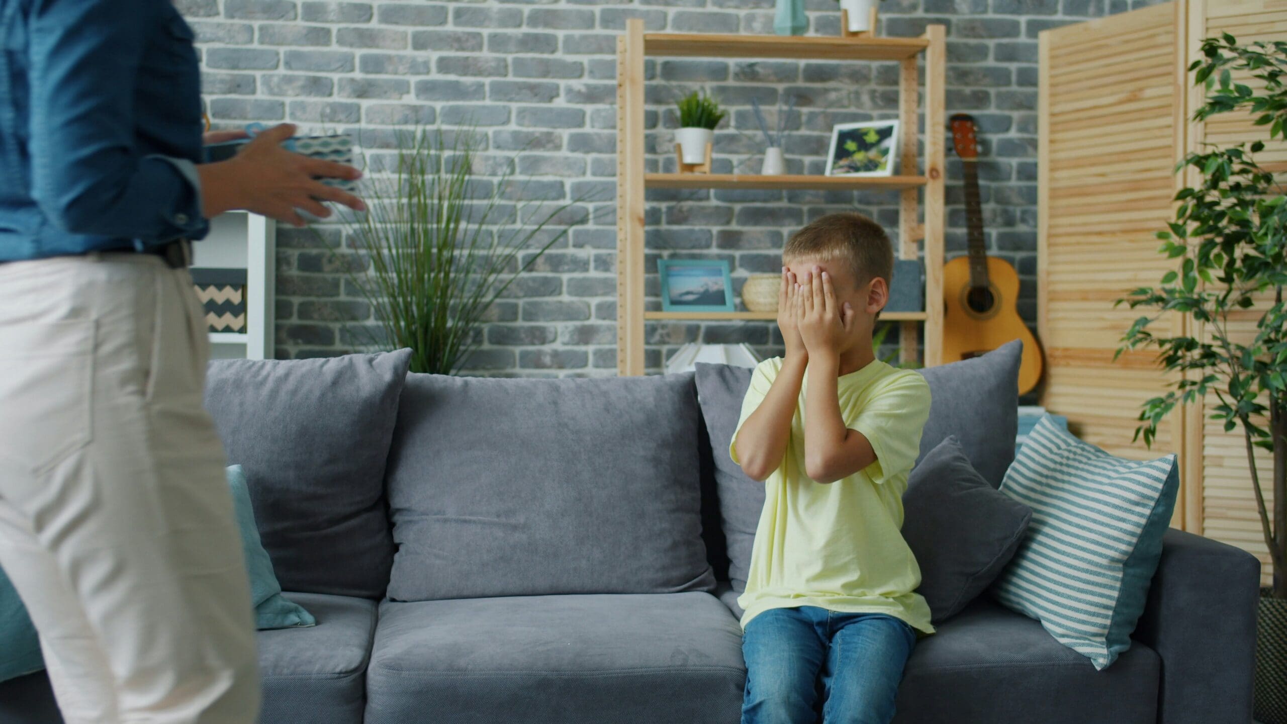 Child hiding face while adult stands nearby