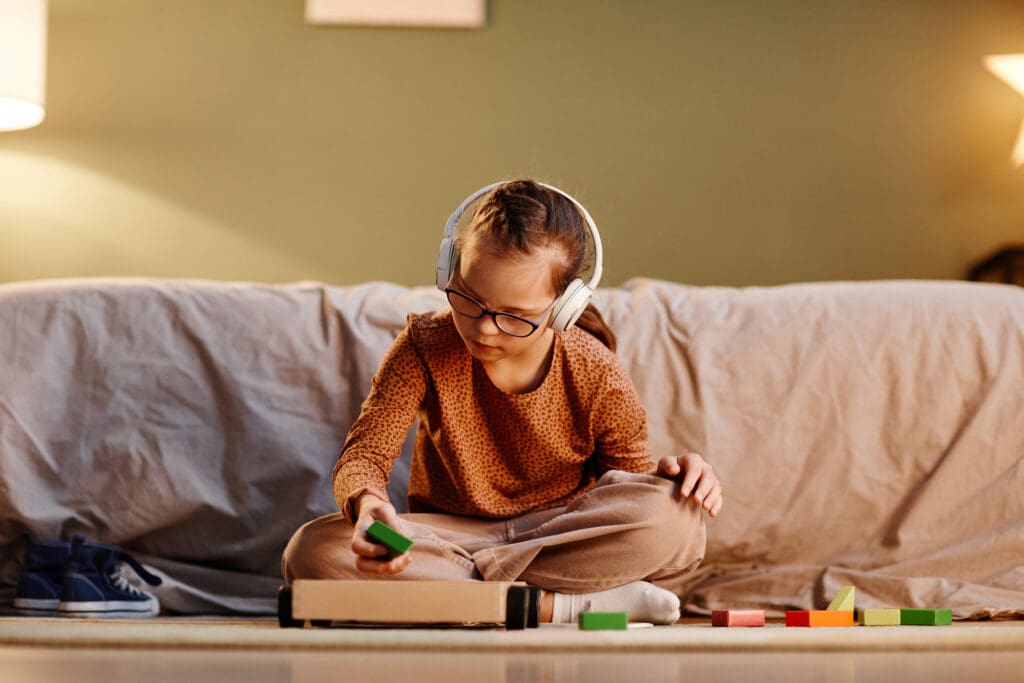 A young girl playing with blocks and wearing noise cancelling earphones.
