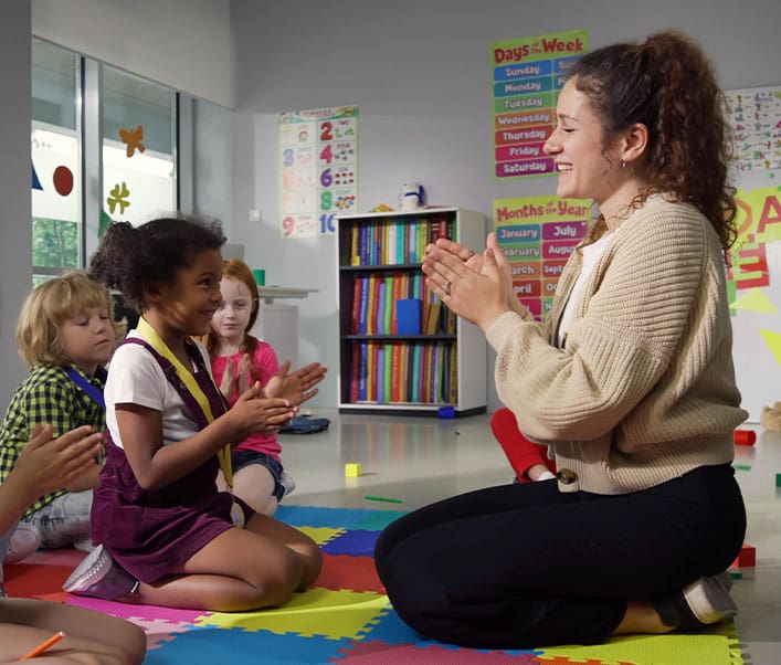 Proud teacher giving medal to preschool girl at classroom
